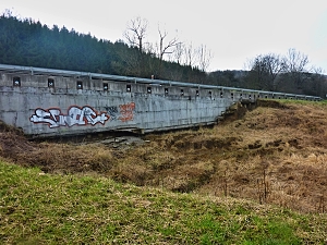 Pohled od potoka na sesuvem obnaženou opěrnou zeď silnice /foto:RSZK